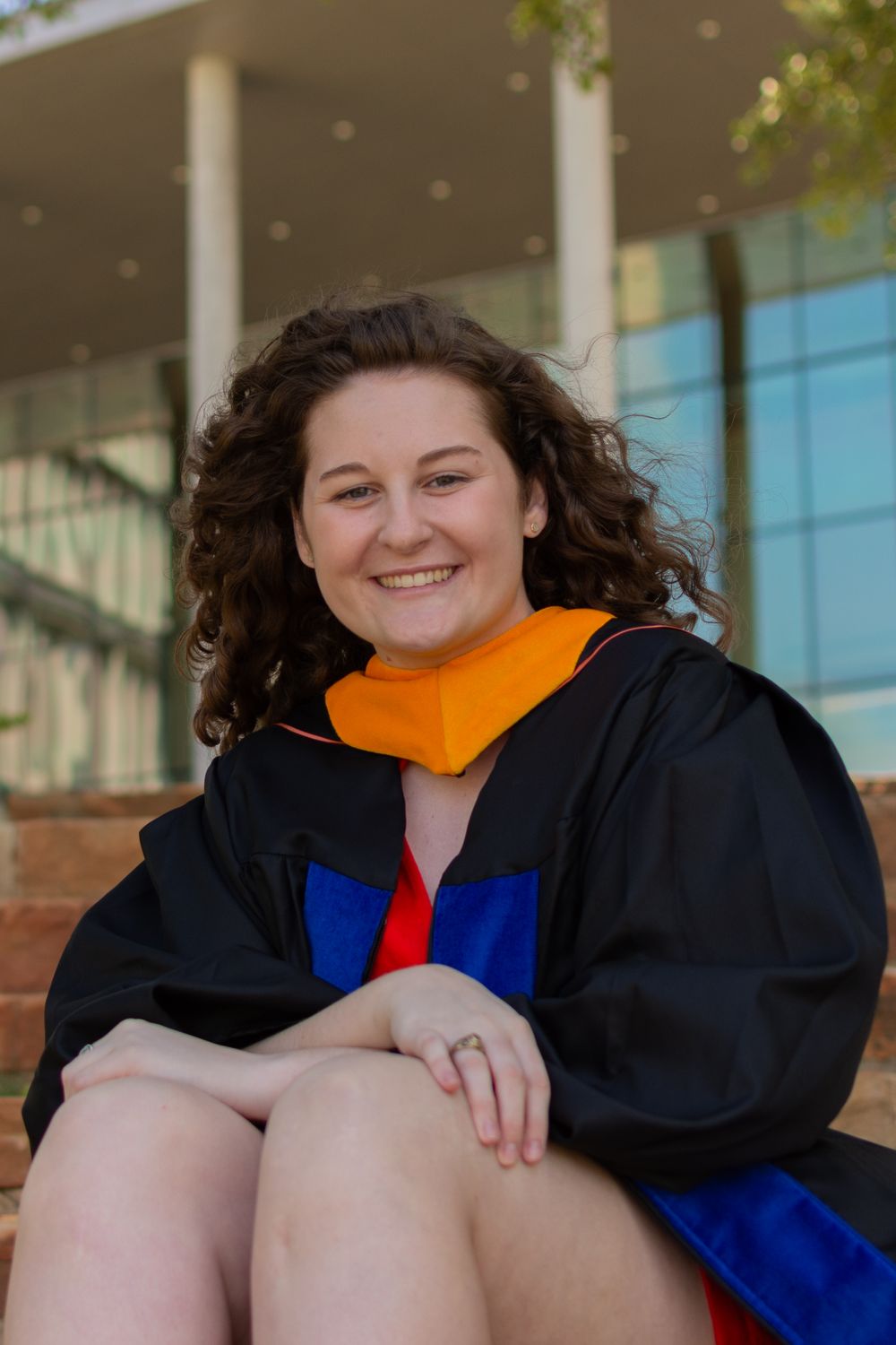 UT Arlington Masters graduate student smiles as she sits while wearing her grad gown and academic hood.