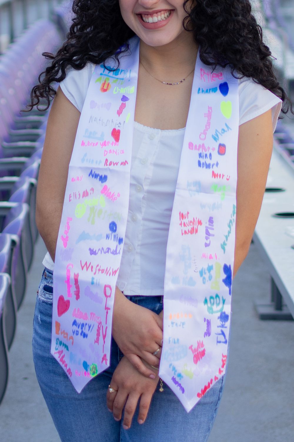 Close-up of a TCU grad's stole signed in fun colors by her students. She's standing among the purple, horned frogs football stadium seats.
