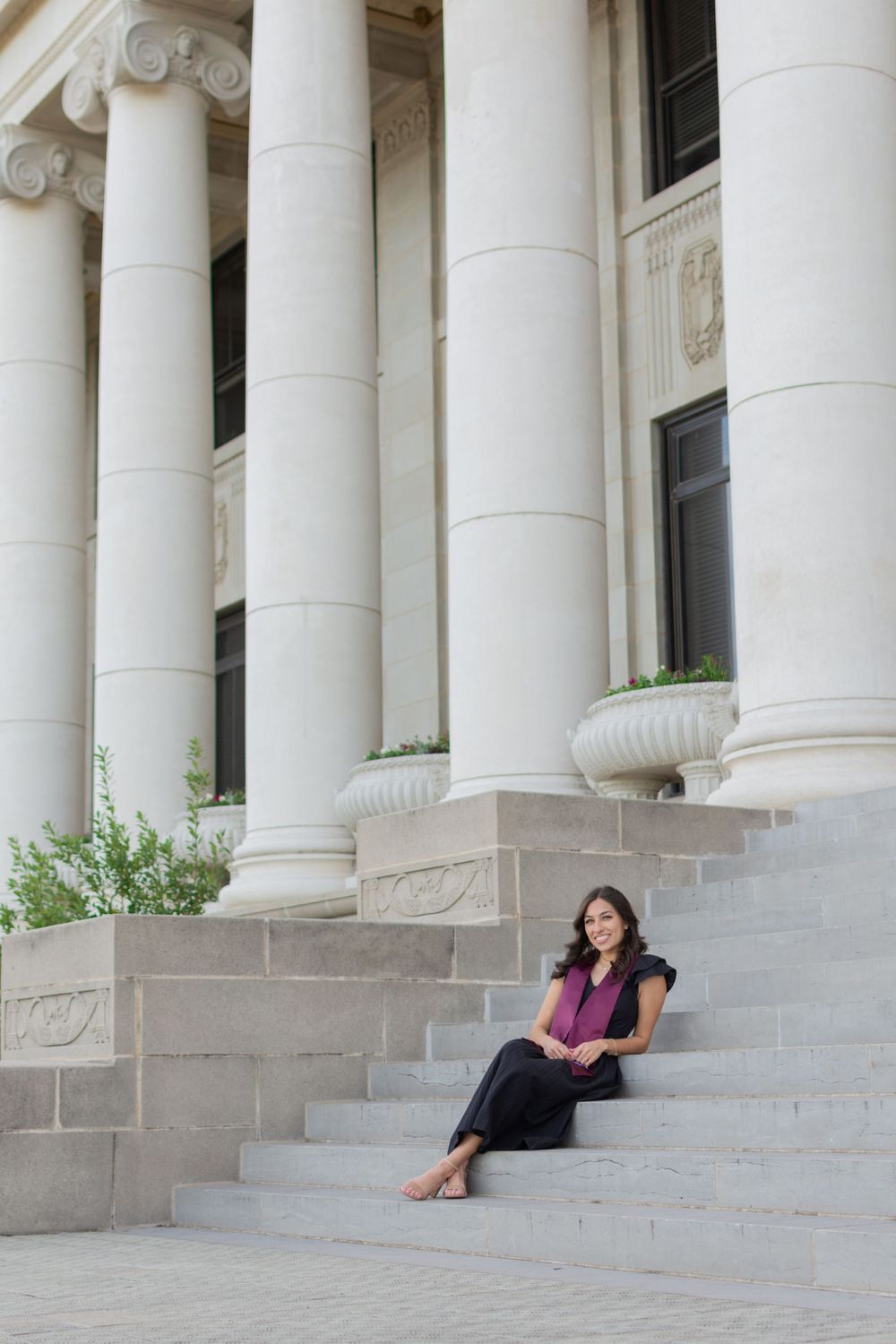 TAMU senior sits on the steps of the Administration Building during her grad photoshoot in winter. She wears a black midi dress & nude heels