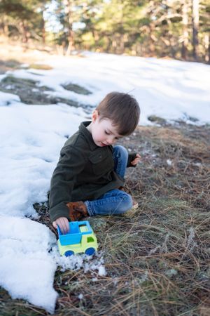 Child plays with toy truck in snowy outdoor setting.