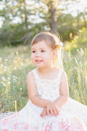 Child in white and pink floral dress poses outdoors during sunset.