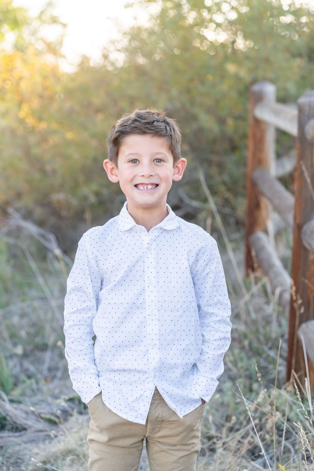 Young person wearing white polka dot shirt and khaki pants standing outdoors in natural setting.