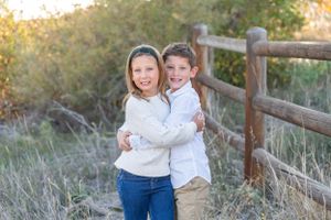 Children having fun and hugging outdoors by a rustic wooden fence at golden hour.