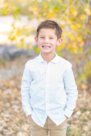 Person in polka dot shirt and khaki pants smiling outdoors with autumn colors in background.