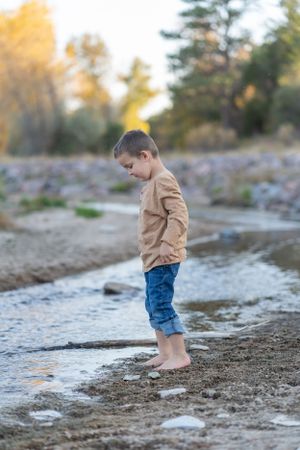 Person testing water with bare feet at river's edge in autumn.