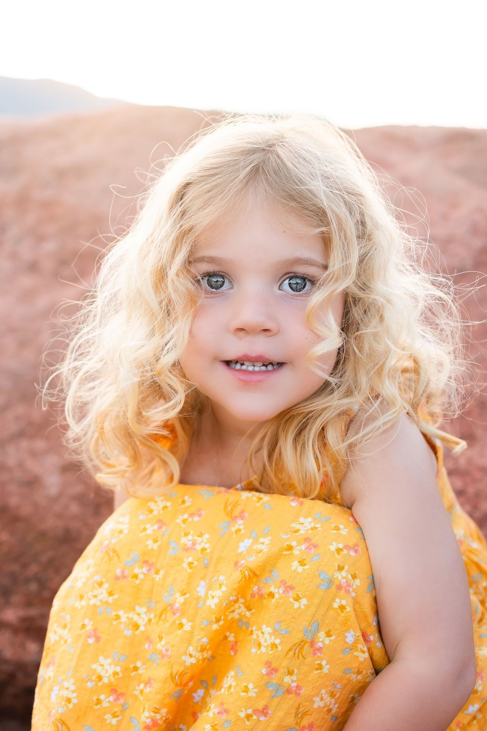 Young child in yellow floral dress against red rocks at sunset.