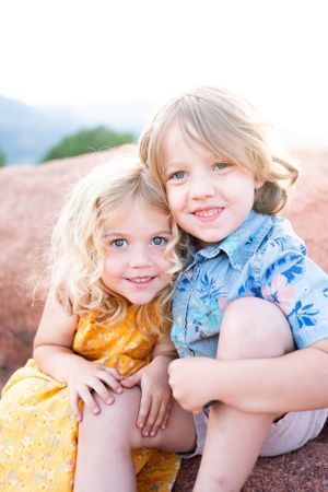 Two young children sitting together on red rocks during golden hour.