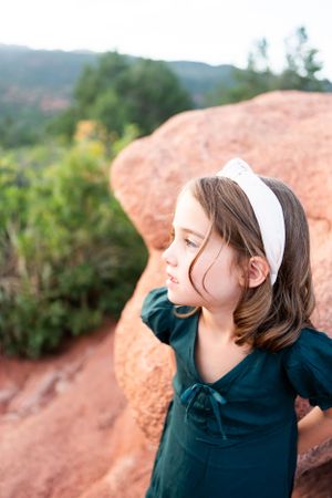 Child in navy dress with white headband looking at scenic mountain vista.