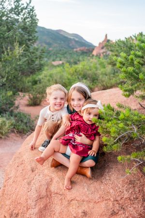 Three children sitting together on red rocks with Garden of the Gods in background.