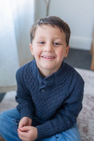 Child in navy cable knit sweater smiling and posing on patterned surface.