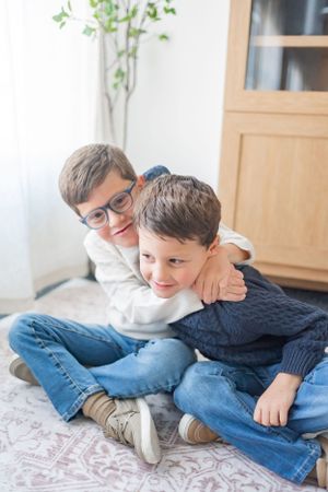 Two children in sweaters playfully interacting on patterned carpet.