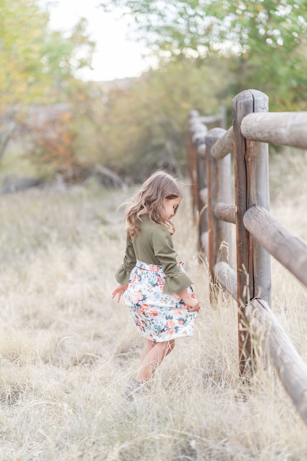 Person in floral skirt twirling by rustic wooden fence during autumn.