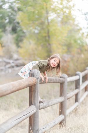 Person playfully lying on wooden fence in autumn field.