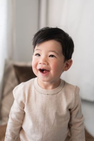 Joyful child in beige sweater laughs against light interior background.