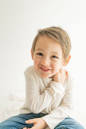 A young child in a white sweater smiles sweetly while sitting against a light background.