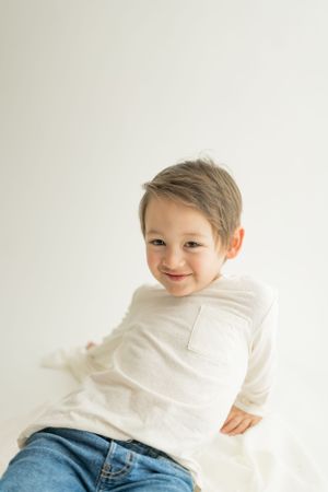 Child wearing a white long sleeve shirt and jeans poses playfully against a white backdrop.