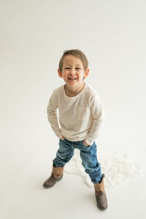 Energetic child in boots and jeans strikes a fun pose while wearing a white sweater.