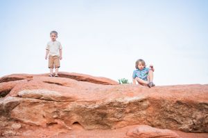 Children playing on red sandstone rock formations against blue sky background.
