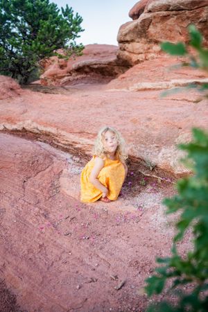 Person in bright yellow dress sitting on red rocks surrounded by greenery.
