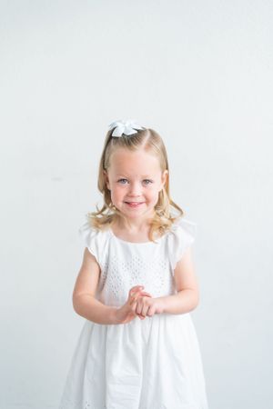 Young girl in white eyelet dress smiling against plain white background.
