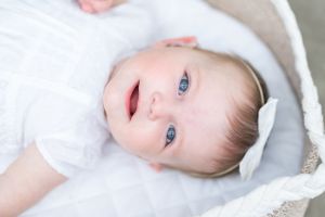 Close up portrait of baby with blue eyes wearing white outfit laying on soft surface.