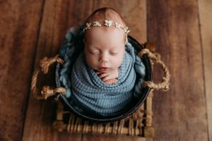 Professional newborn portraits with baby wrapped in gray knit against wooden backdrop.