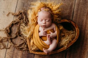 Artistic newborn photography series with mustard yellow wrap on rustic wooden background.