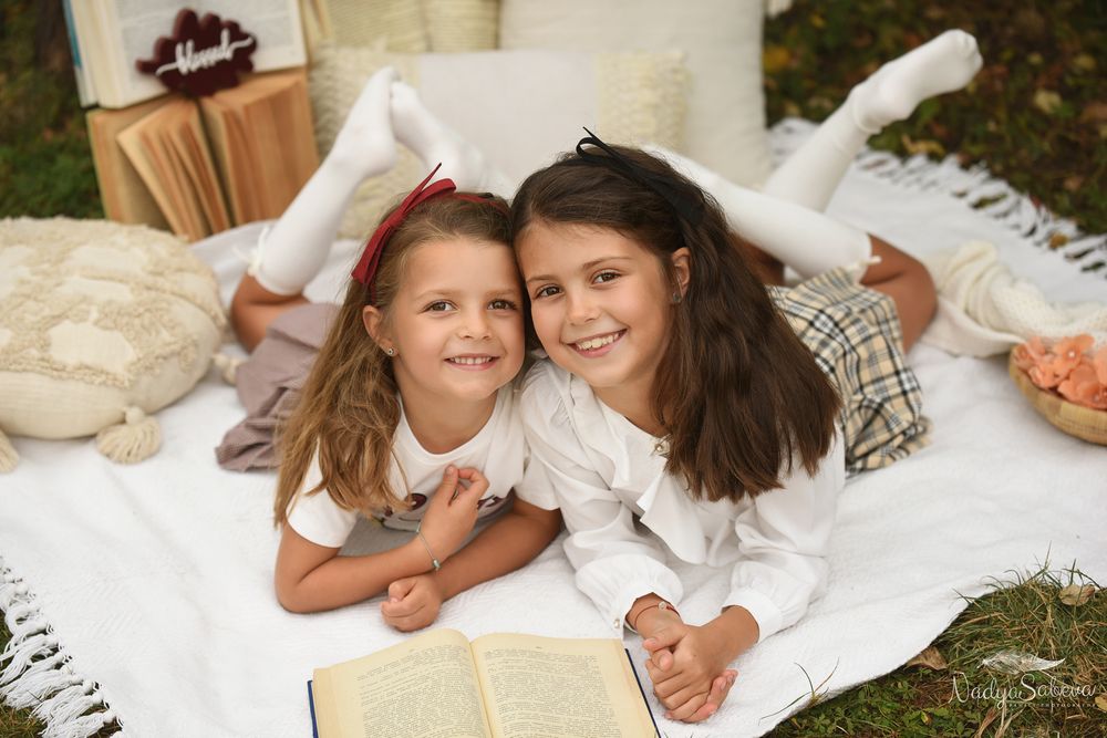 Two people wearing white clothing lay on white blankets outdoors while sharing a joyful moment together.
