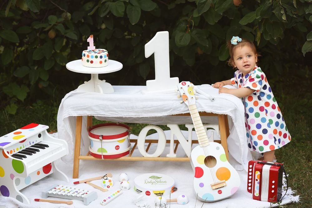 A colorful first birthday party setup with white furniture, polka dot decor, and musical instrument themed accessories.