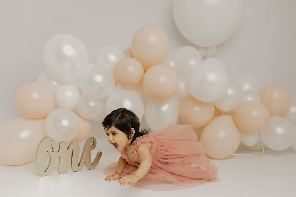 Elegant maternity photos with white and peach balloon arch and soft pink dress.