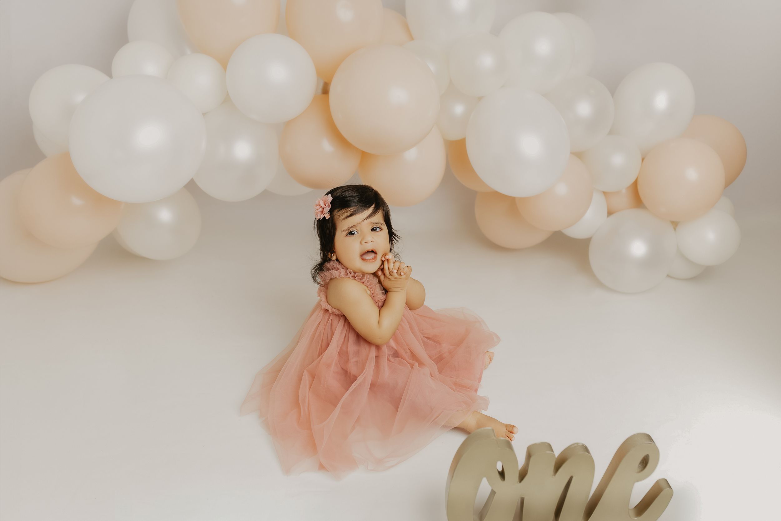 Dreamy maternity portraits with blush dress against white and peach balloon backdrop.