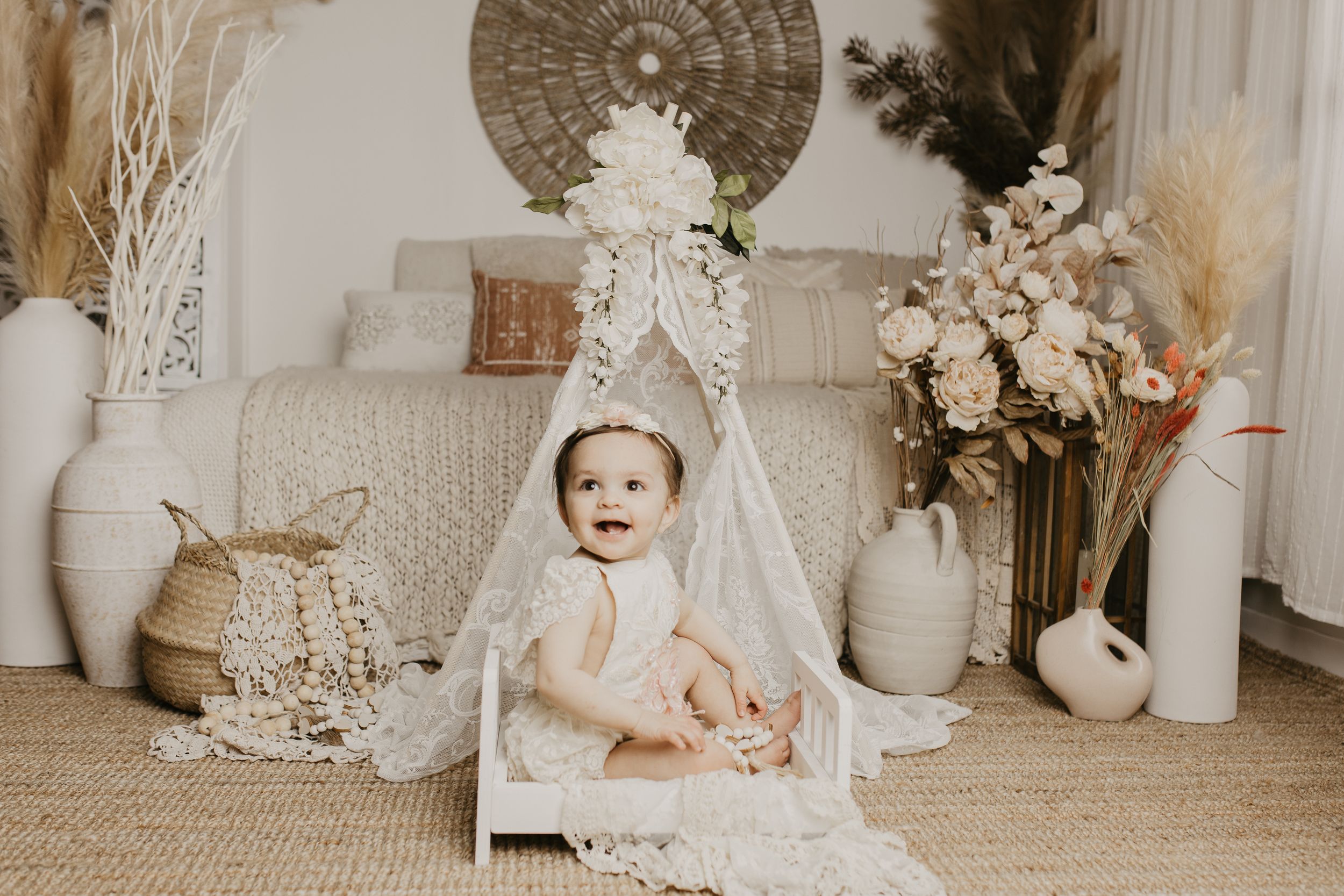 Artistic maternity photoshoot setup with neutral tones, dried flowers, and decorative elements.