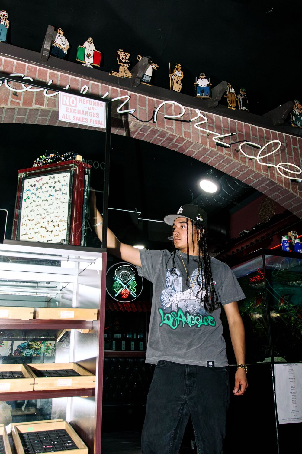 Tattoo artist with dreadlocks standing inside Brown Pride Tattoos shop with cultural decor.