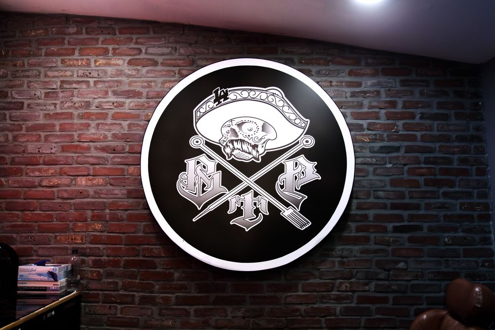 Brown Pride Tattoos circular logo on brick wall featuring skull and crossed tattoo machines.