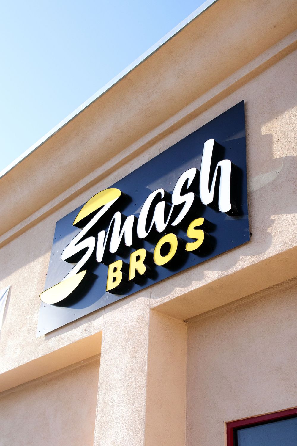 Smash Bros restaurant exterior sign with bold black and yellow branding against blue sky.