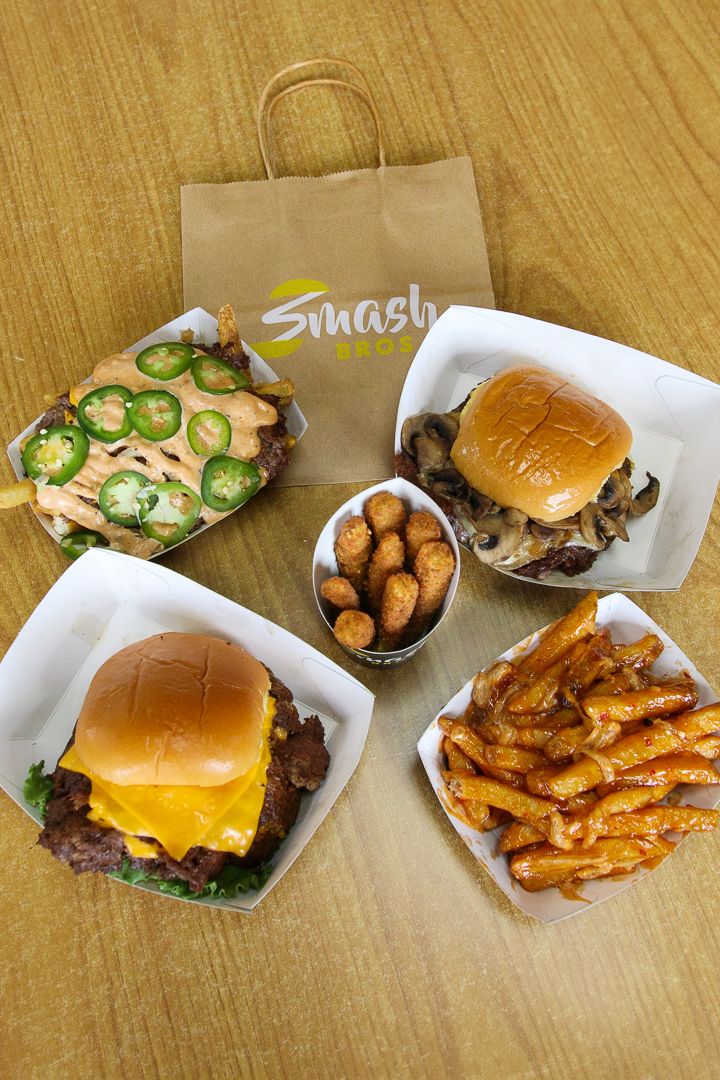 Smash Bros burger meal spread with fries, tater tots, and takeout bag on wooden table.