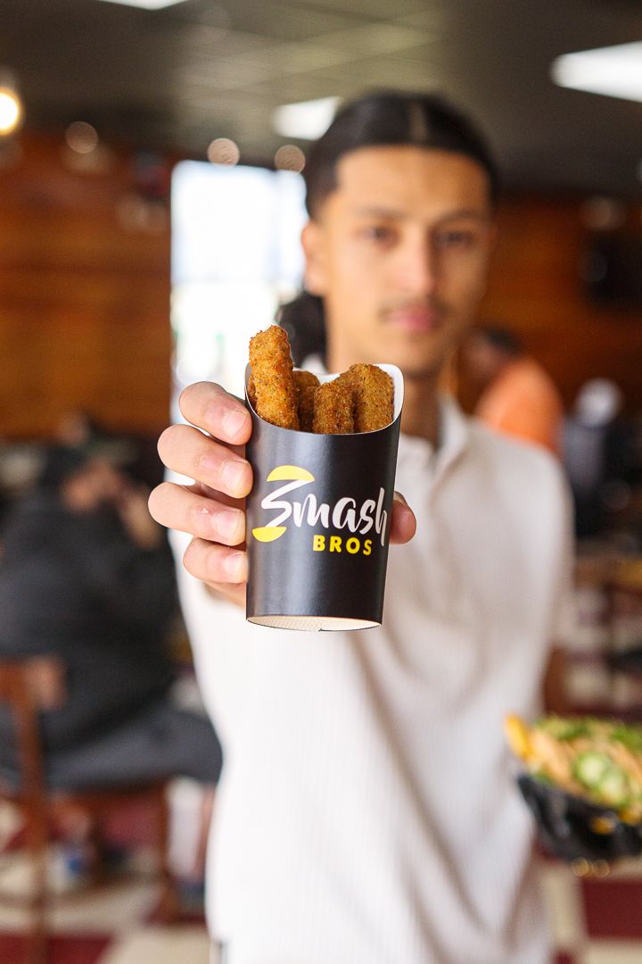 Man holding Smash Bros branded cup with fried food inside at a restaurant.