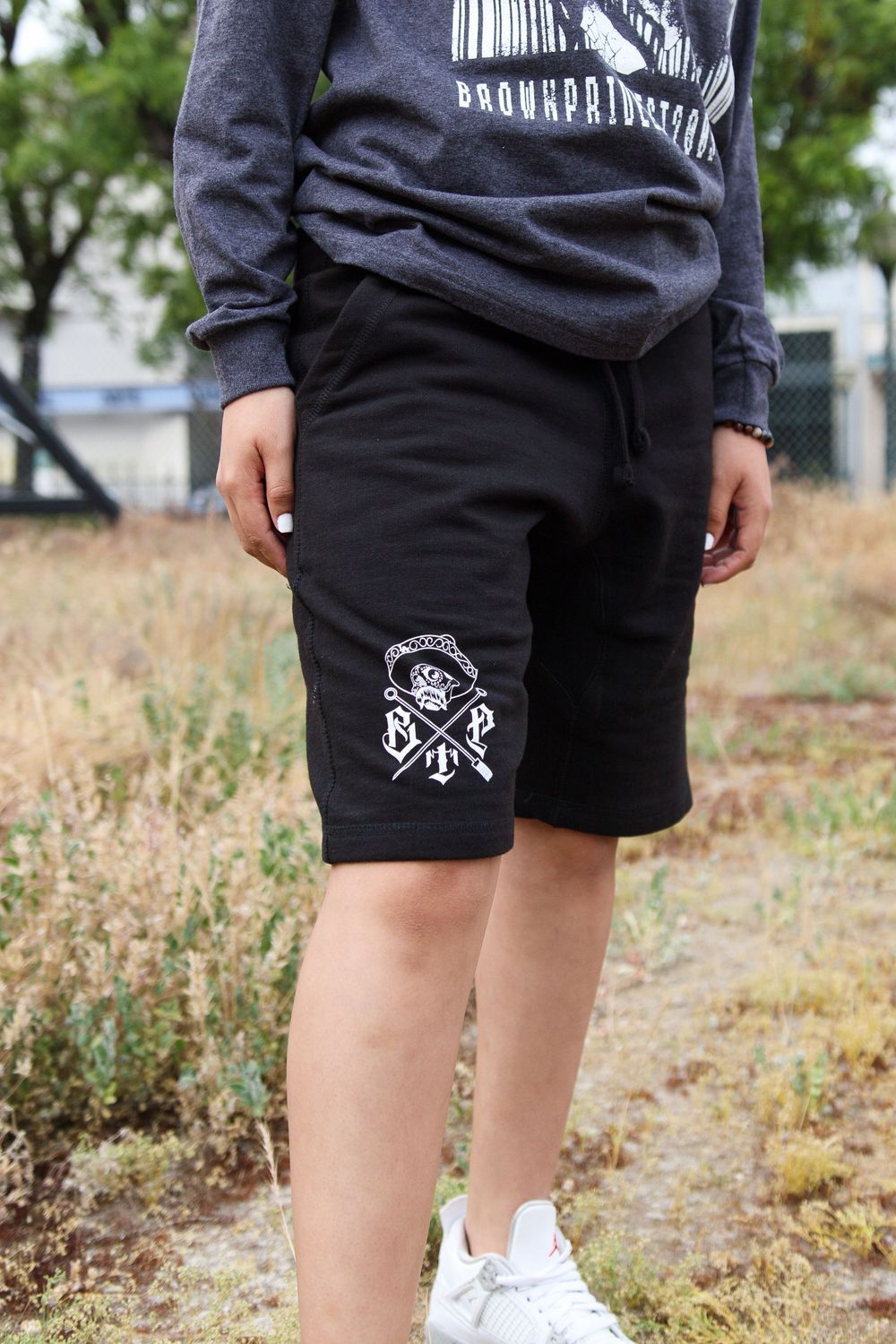 Close-up of black shorts with Brown Pride logo worn with gray hoodie and white sneakers.