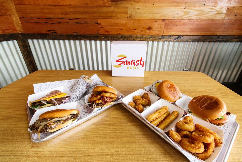 Smash Bros restaurant spread featuring smash burgers, onion rings, and sides on a wooden table.