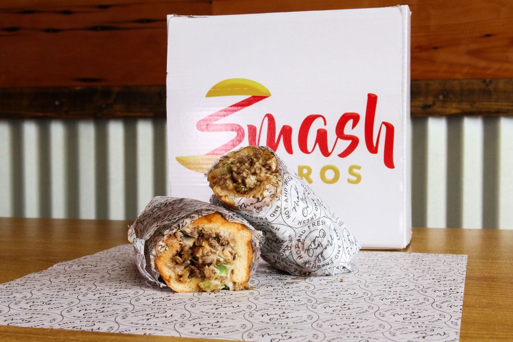 Smash Bros burrito cut in half revealing savory filling, displayed in front of branded white box.