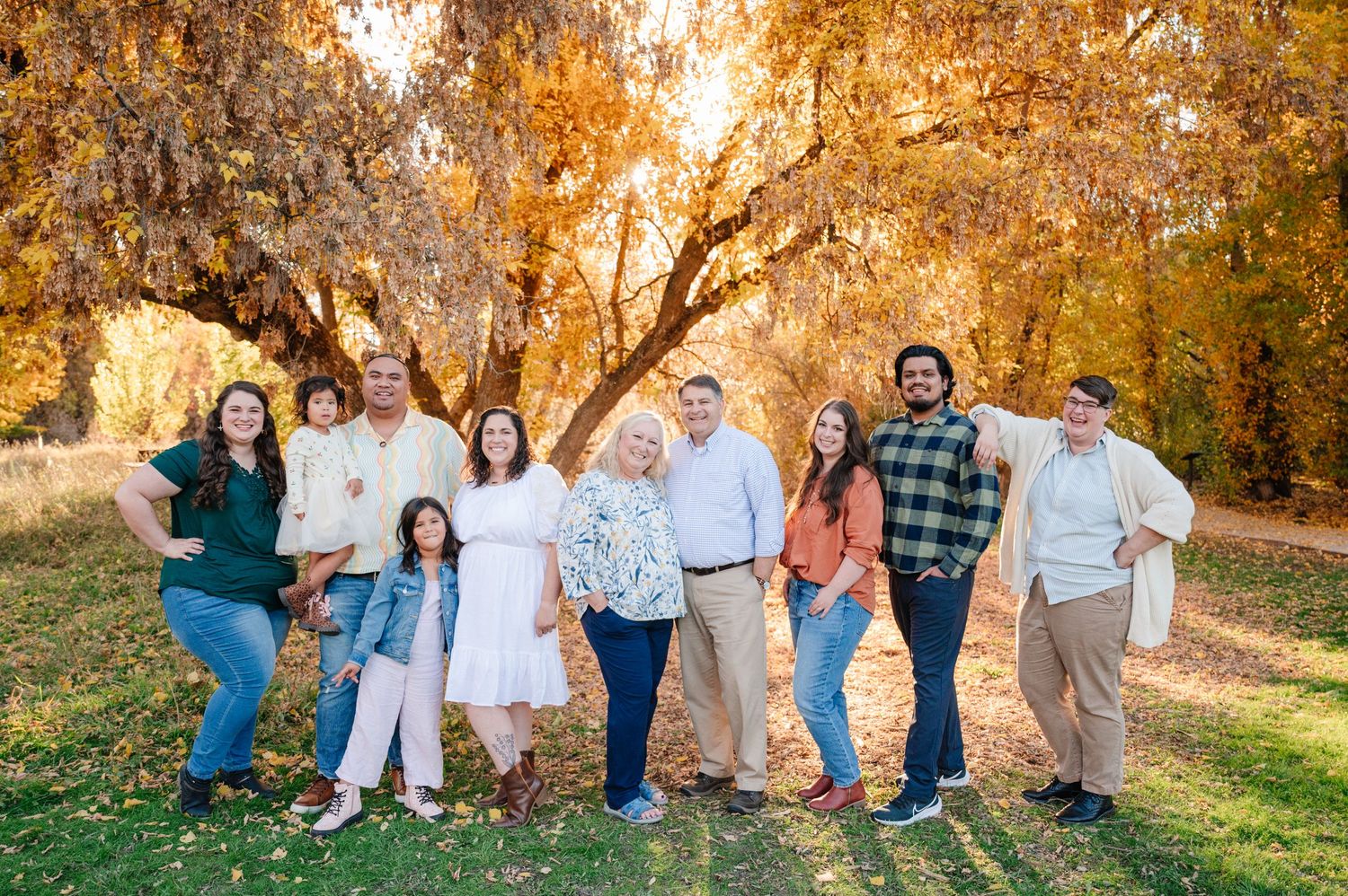 Extended family gathering outdoors in autumn with golden sunlight filtering through trees.