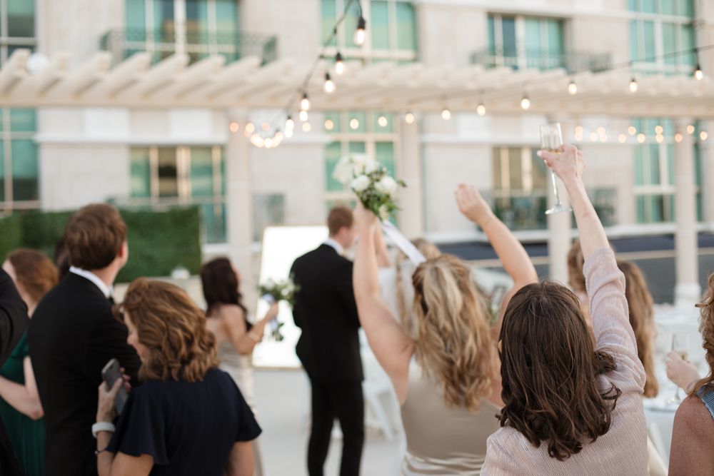 Wedding guests raising hands in celebration at outdoor rooftop ceremony with string lights.