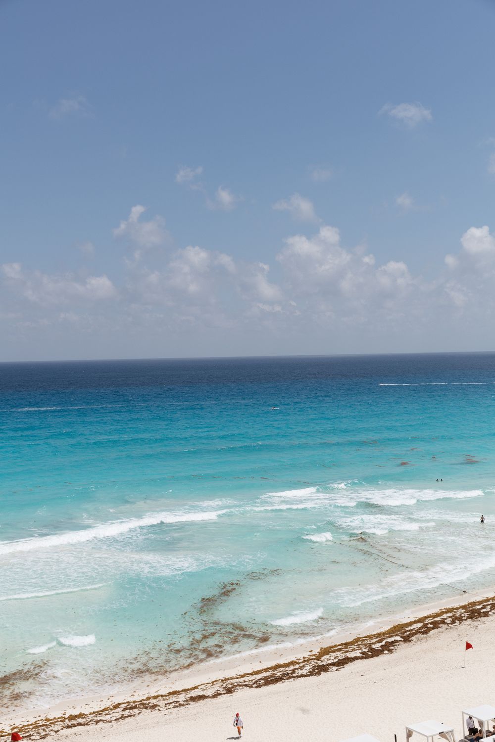 Aerial view of a stunning turquoise Caribbean beach with white sand, gentle waves, and a clear blue sky.