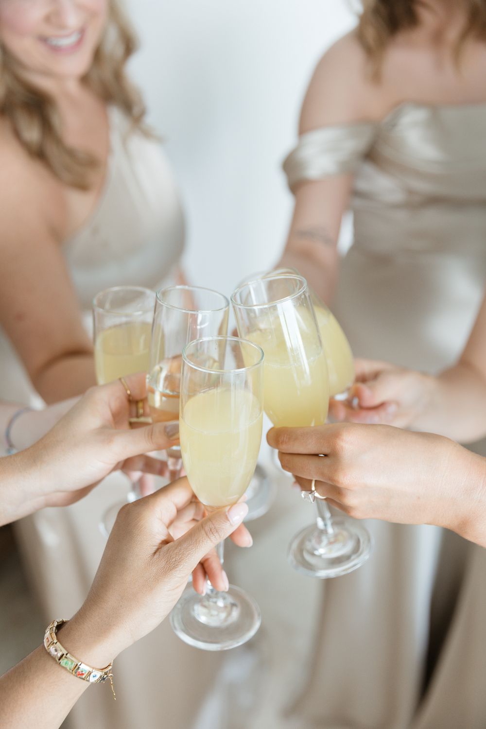 Bridesmaids in champagne dresses toasting with glasses of mimosas at a wedding celebration.