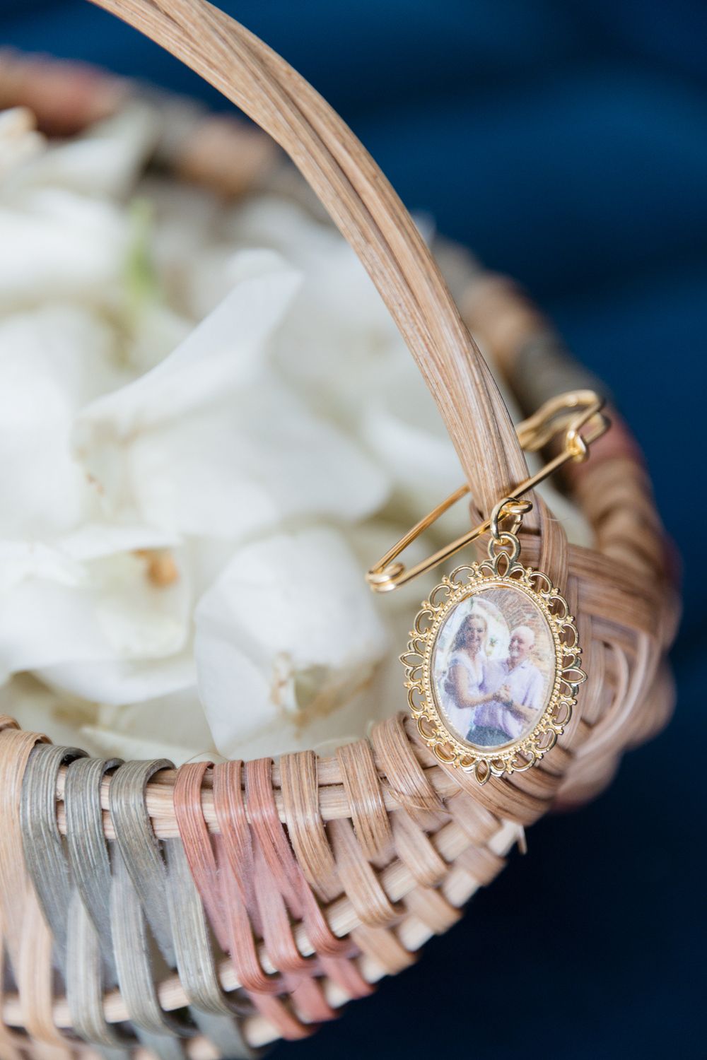 Wicker flower basket with white rose petals and gold oval photo memorial charm pinned to the handle.