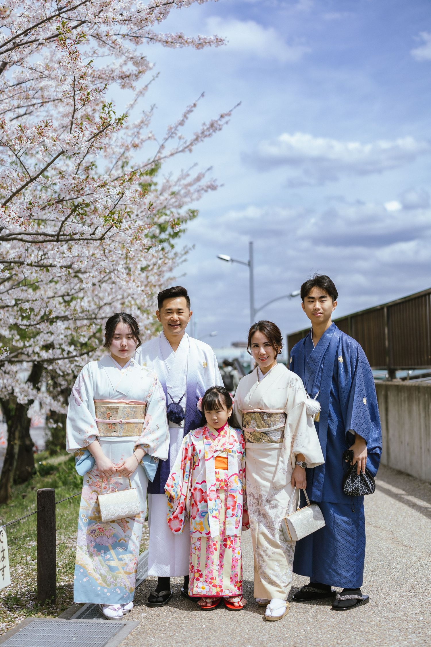 A family wearing traditional Japanese kimono and yukata poses together under blooming cherry blossoms.