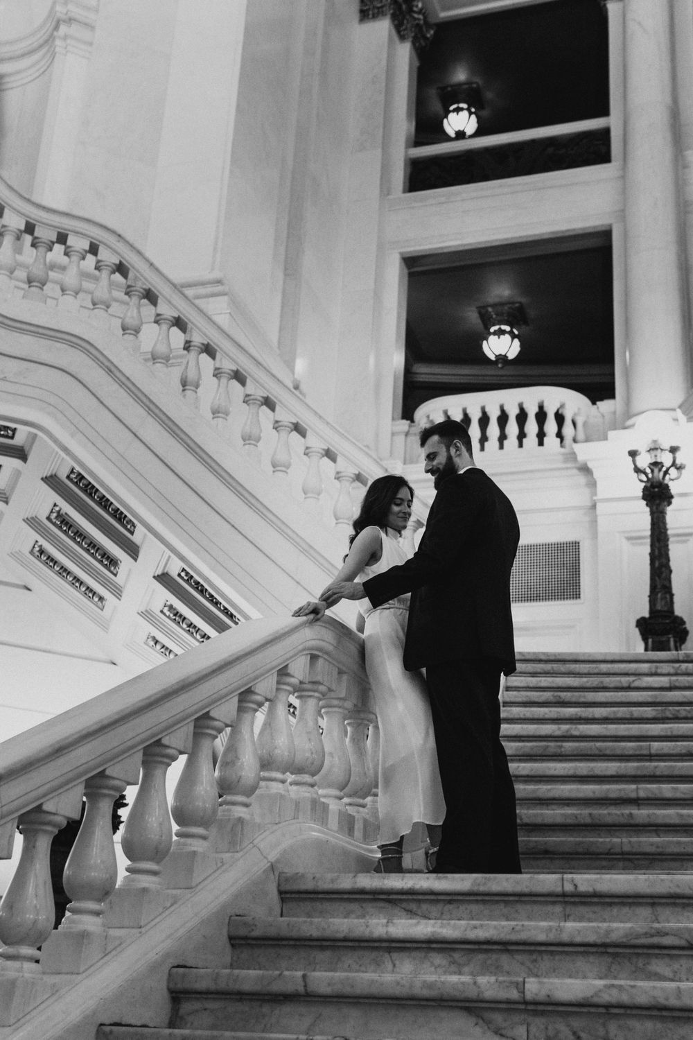 A black and white photo of a couple sharing an intimate moment on an elegant staircase.