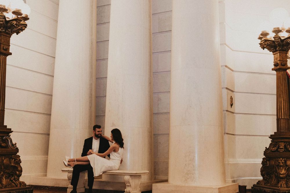 A couple shares a romantic moment while seated on marble steps in an elegant venue.