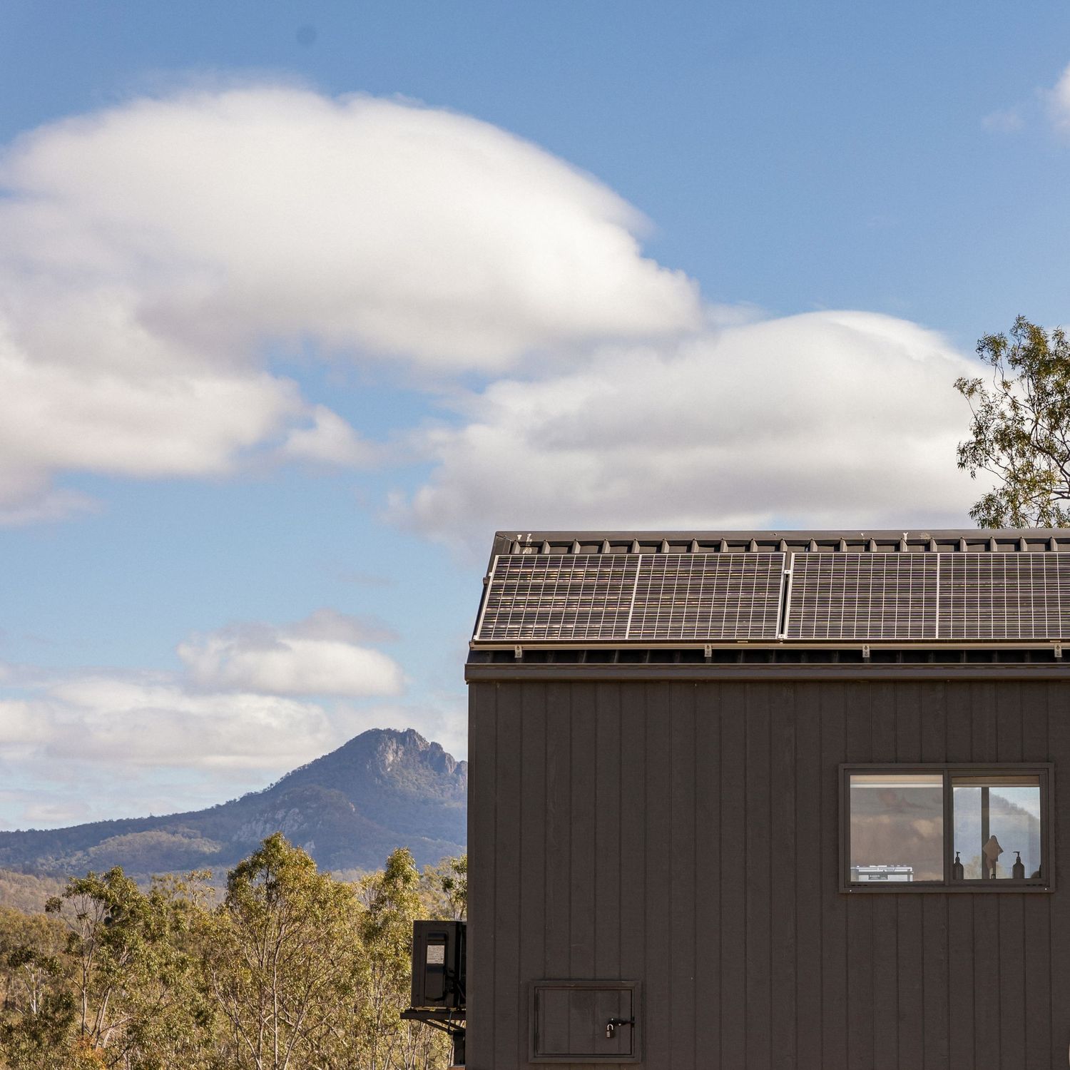 Modern tiny house with solar panels against mountain backdrop and blue sky. Unyoked Cabin in Queensland.