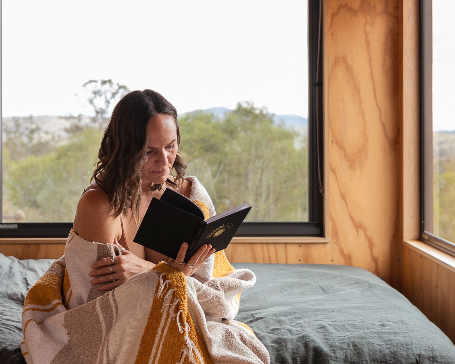 Cozy morning scene of reading in bed by large window with natural light.